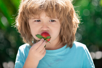 Happy child eats strawberries in the summer outdoor on green spring background. Close up kids happy face.