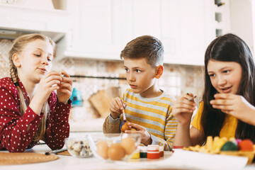 Funny and cheerful children sitting at the table paint Easter eggs in different colors for Easter