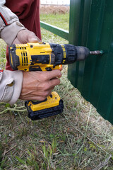 The worker with a screwdriver screws the screws into the fence, installing a metal fence.