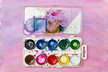 a set of used old watercolors on a pink background copy the space.  a box of watercolors for drawing, a palette. The concept of the artist's creativity