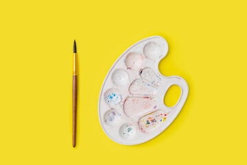 used palette for mixing paints, colors, and a brush for drawing on a yellow background .a set of objects for drawing. The concept of the artist's creativity, hobby