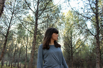 Young brunette girl posing in the forest with trees in the background
