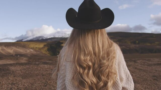 Blond Woman In Cowboy Hat Walking In Icelandic Landscape