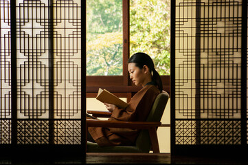 Serene young woman reading book behind patterned shoji doors
