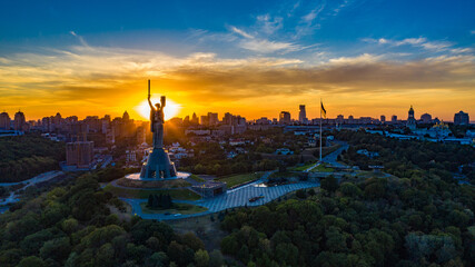 Fototapeta na wymiar Aerial view to the Motherland statue in the Kiev while summer sunset. The well-known landmarks in Kyiv. Historical monument of Soviet union. Beautiful city Kiev while sunset.