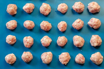 Raw shaped meatballs in sunbeams on blue.