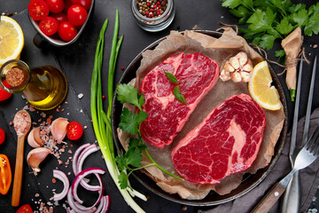 Meat raw steaks with seasoning and herbs on dark background.