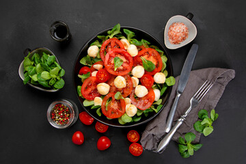 Delicious Italian caprese salad with sliced tomatoes and mozzarela on dark background.