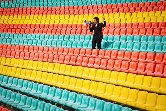 Man with megaphone in colorful soccer stadium seats

