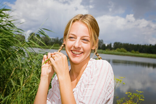 Portrait happy young woman with blonde braids at sunny lake
