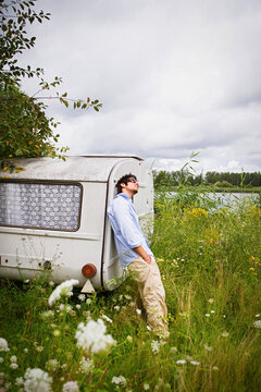 Young man at camper trailer in idyllic lakeside meadow
