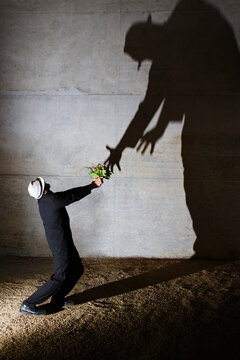 Man offering flowers to tall ominous shadow on wall
