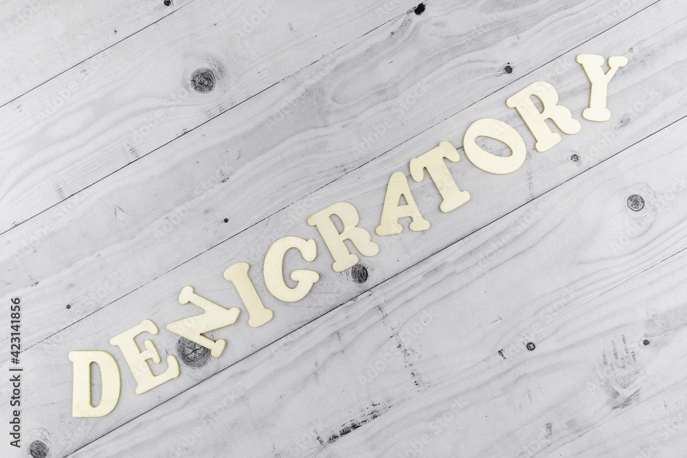Fototapete denigratory - concept with alphabet letters on a diagonal light grey wooden board background with la