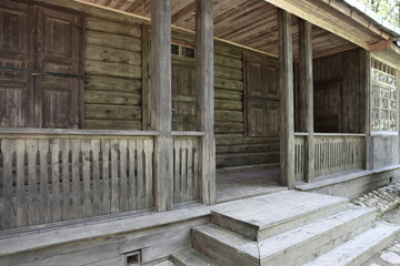 Empty terrace with closed door and window with shutters on traditional ancient Russian log cabin old wooden house at summer day