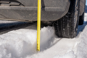 Measuring the vehicle's ground clearance with a ruler. Evaluating the vehicle's off-road capabilities. Winter track. Snow ruts. Sunny day