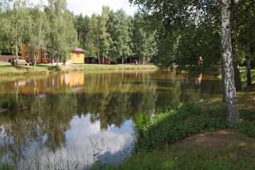 Obraz premium Beautiful forest lake with birch tree and wooden house reflection on the water at Sunny summer day, European natural countryside landscape