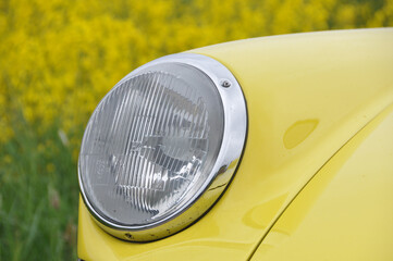 close-up of a headlight of a yellow vintage oldtimer car in field of rapeseed