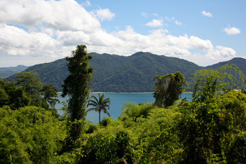 Nosy Be Island and its mountains covered with green vegetation seen from the Nosy Komba jungle with the Indian Ocean in the middle. View of Lokobe Reserve and the white sand line of the coast.