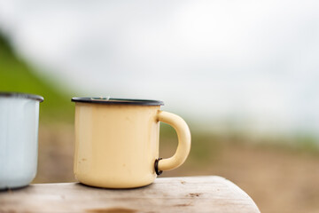 Outdoor tourism and recreation concept. two iron mugs stand on a log against the backdrop of sky and nature.