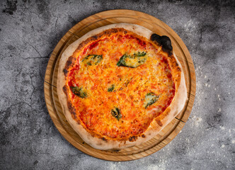 Four cheeses pizza with basil leaves on a round wooden pizza board.