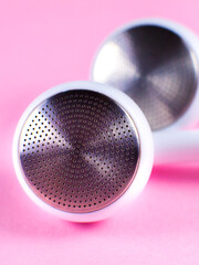 White Earphones lying on the pink background. Modern music concept. Audio technology. Close up photo.