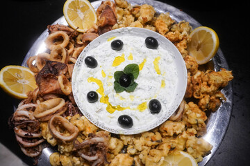 Plate with squid, shelled bread and tsatsiky sauce, garnished with olives and basil leaves. Product photography.