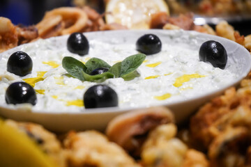 Plate with squid, shelled bread and tsatsiky sauce, garnished with olives and basil leaves. Product photography.
