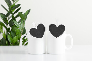 Two mugs mockup with workspace accessories, green plant on white table. Front view. Place for text, copy space, mockup