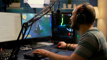 Streamer man wearing headset start to play online space shooter video games. Pro e-sport player playing gaming tournament on RGB computer, using modern streaming technology