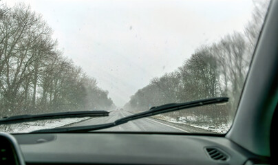 Car wipers wiping the windshield. Winter highway during snowfall	