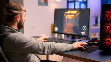 Caucasian man playing online video games for virtual championship using professional RGB system desktop. Pro gamer siiting on gaming chair looking and smiling at camera late at nigh in home studio.