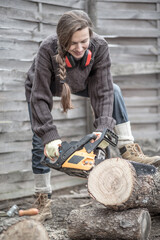 Young woman with a chainsaw. Female builder blogger showing how to saw wooden log