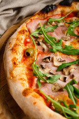 Close up pizza with arugula, mushrooms, prosciutto and olives.