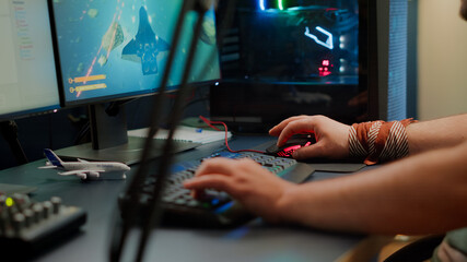Close up of player hands using RGB keyboard in gaming home studio streaming space shooter game. Digital gamer using professional equipment for video game competition late at night in living room © DC Studio
