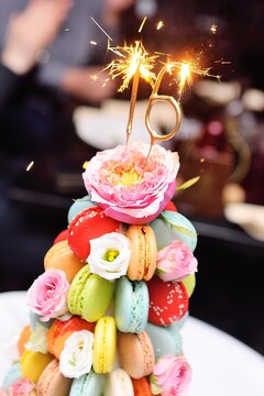sparklers or burning candles on a birthday cake for the sixteenth birthday of macaroons and flowers close-up.