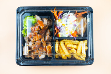 Grilled pork steak with vegetable salad, mashed potatoes and french fries in takeaway box