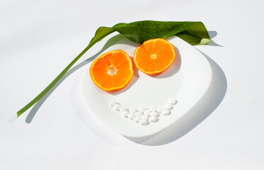 Orange slices are two eyes. The white pills are the mouth. The green leaf is the hair. The plate is this face. Healthy food and supplements theme.