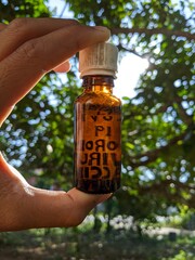 A man is holdings a vaccine bottle with blurred trees on background at the garden