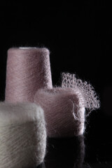 Skeins with pink and beige yarn on a black background.The concept of hobby knitting. Fluffy yarn.Free space.Natural wool mohair. Handmade work.Vertical photo.