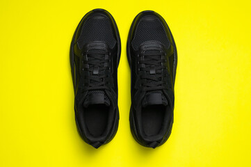 Black classic men's sneakers on bright yellow background. Fashionable youth sports sneakers. Sports casual shoes. Footwear for fitness, running, healthy lifestyle. Flat lay top view copy space