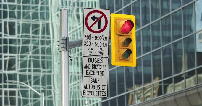 Traffic signals head and pole on Red with a no left turn sign, in the background there is a beautiful window covered high rise in the background in Ottawa, Canada. 
