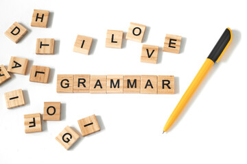 Top view of pen and word grammar made of square wooden tiles with the English alphabet scattered on a white background with space for text. The concept of thinking development, grammar.