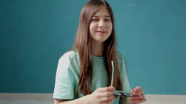 Portrait of smart schoolgirl with long brown hair wearing glasses.  Concept of eye fatigue and ophthalmic problems. Slow motion 50 fps
