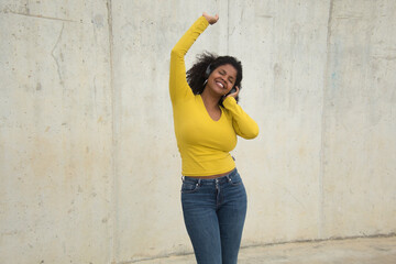 African american woman with afro hair and yellow t-shirt and bluetooth headphones dancing happily.