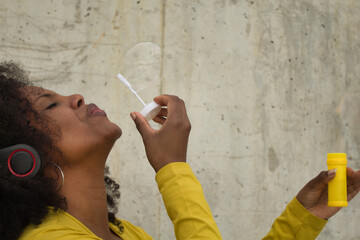 African american woman with afro hair and yellow t-shirt blowing soap bubbles.