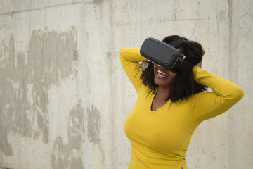 African american woman with afro hair and yellow t-shirt playing with virtual goggles.