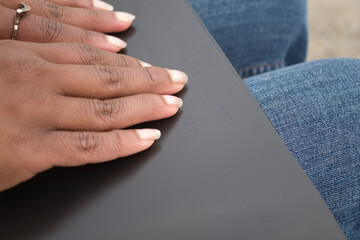 Detail of african american woman´s hands reading braille in a black book.