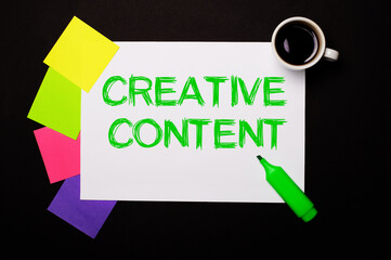 A sheet of paper with the words CREATIVE CONTENT, a cup of coffee, bright multi-colored stickers for notes and a green marker on a black background. View from above.