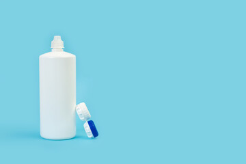 Envase cerrado para lentillas y un bote de solucion para limpieza sobre un fondo celeste liso y aislado. Vista de frente. Copy space