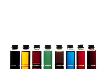 Small bottles with colourful liquid on a reflective surface closed by corks.